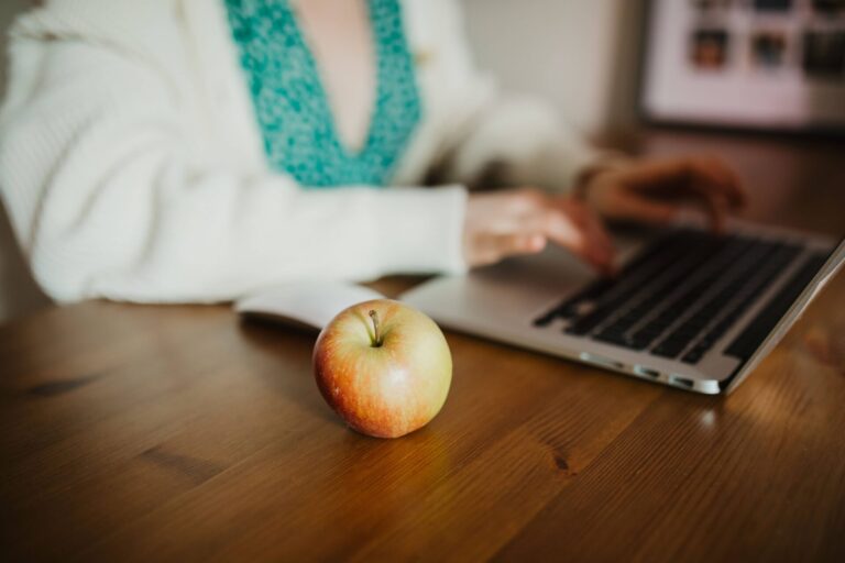 Close up image of a teachers on their computer with an apple on the table