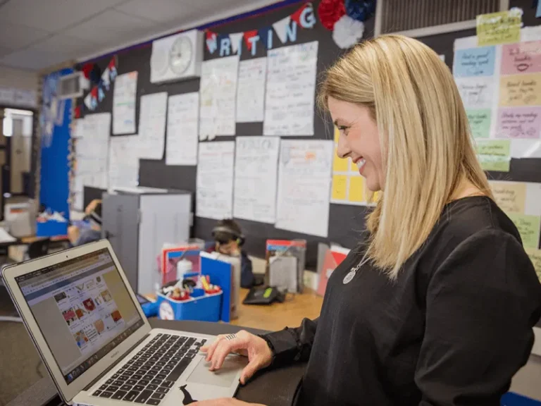 a smiling teacher uses Seesaw on her laptop