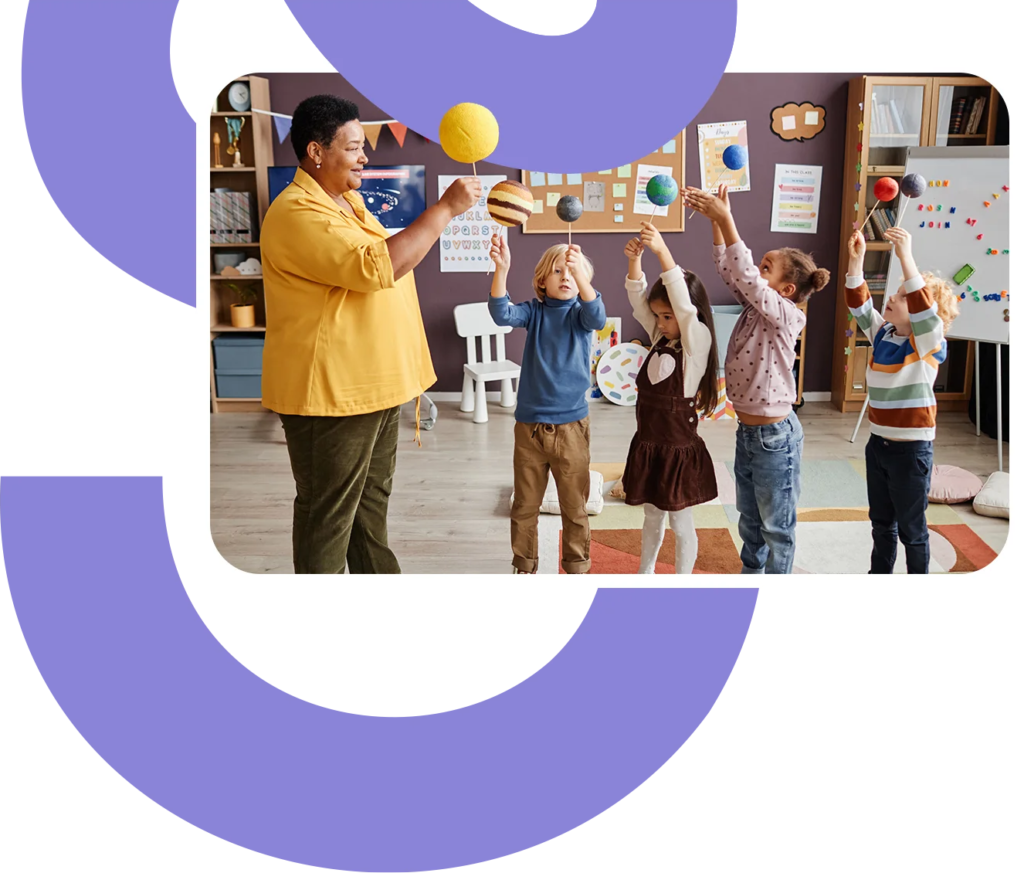 a smiling teacher leads a group of kindergarten students in showing their models of the solar system.