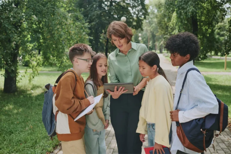 a teacher works outside on a tablet with a group of students