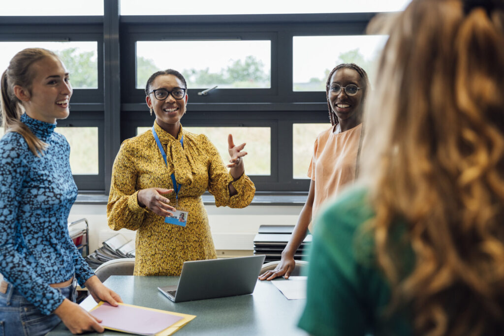 A shot of a mid-adult secondary school teacher talking with her sixth form students in class, they are wearing casual clothing and discussing what they learned in class, in a school in Gateshead, England.