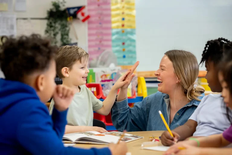 A teacher gives smiling students a high-five during group learning in a colorful elementary school lesson.